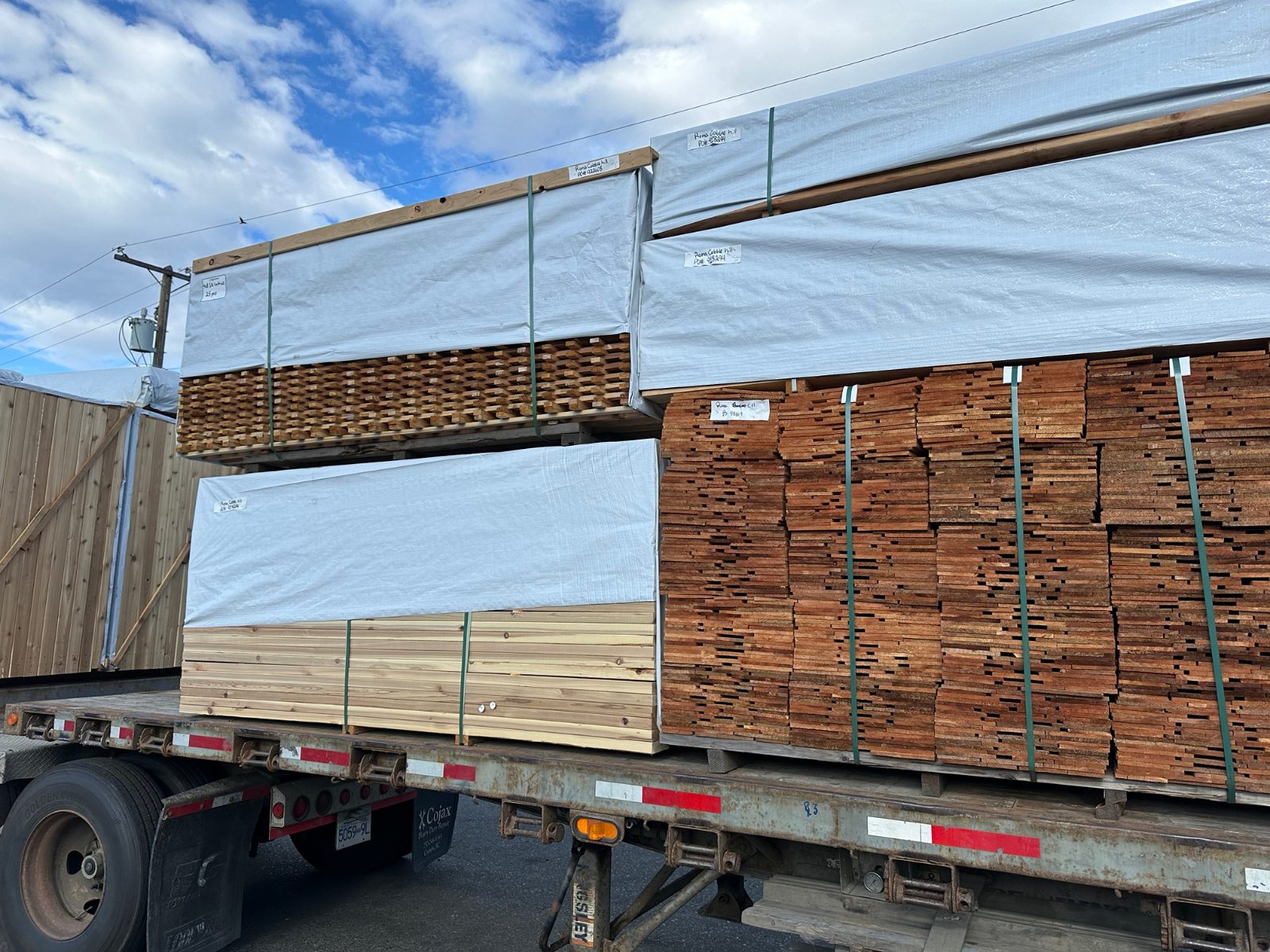 Wrapped packs labelled for a RONA store on a flatdeck: cedar fence boards, lattice and decking